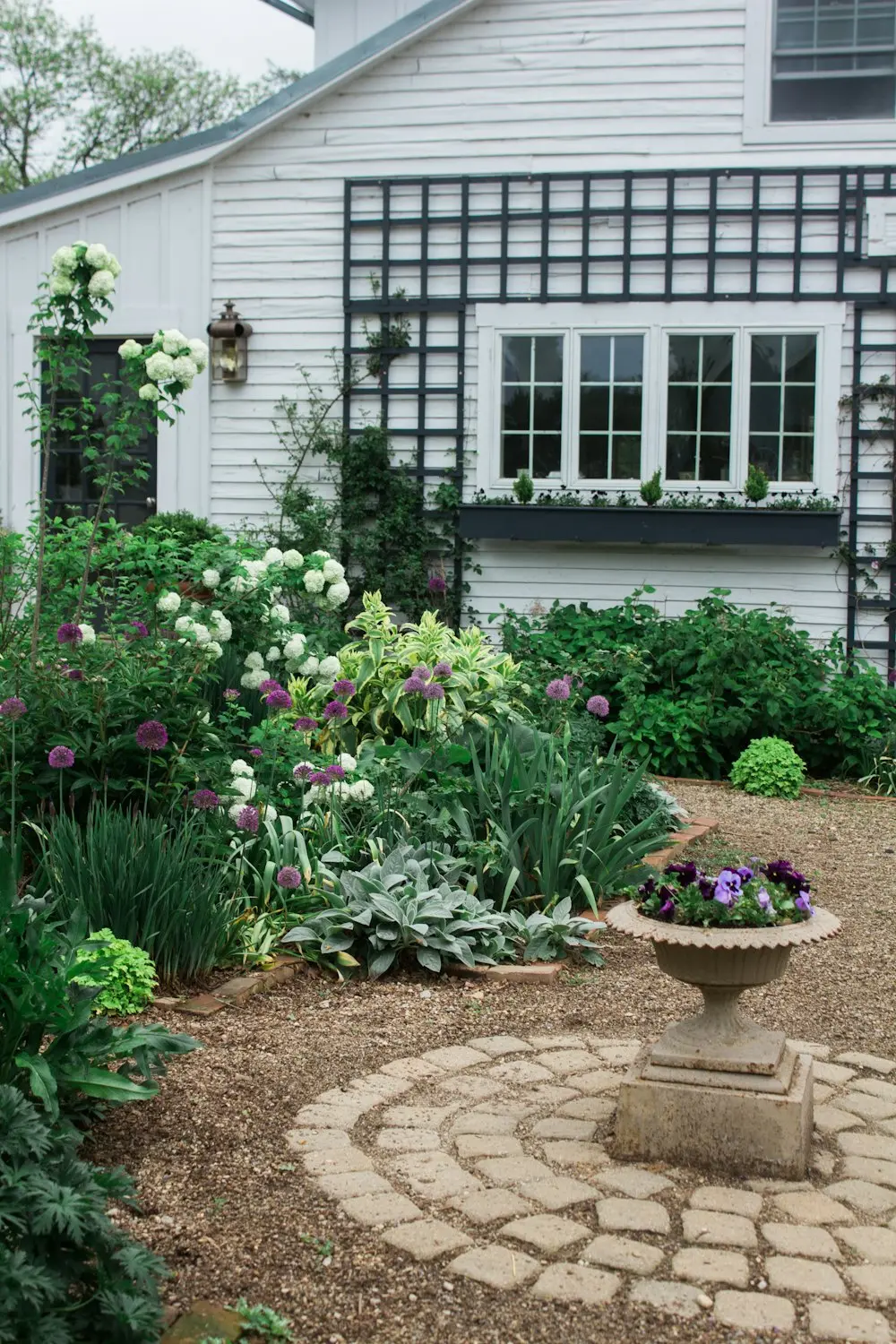 Cottage garden with a circular brick path, stone planter and flowering beds